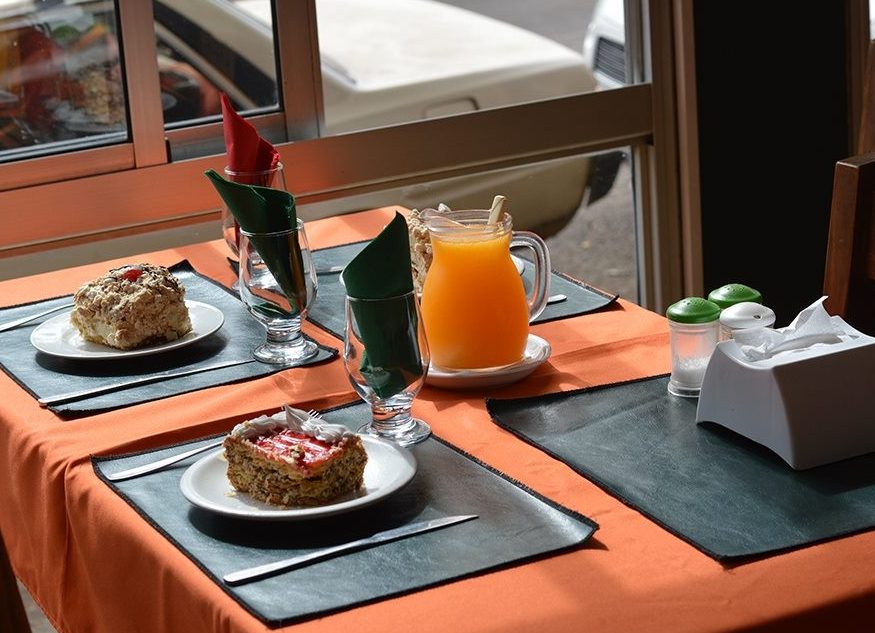 Mesa del salón junto a la ventana, con mantel naranja, dos porciones de postre y una jarra de jugo de naranja